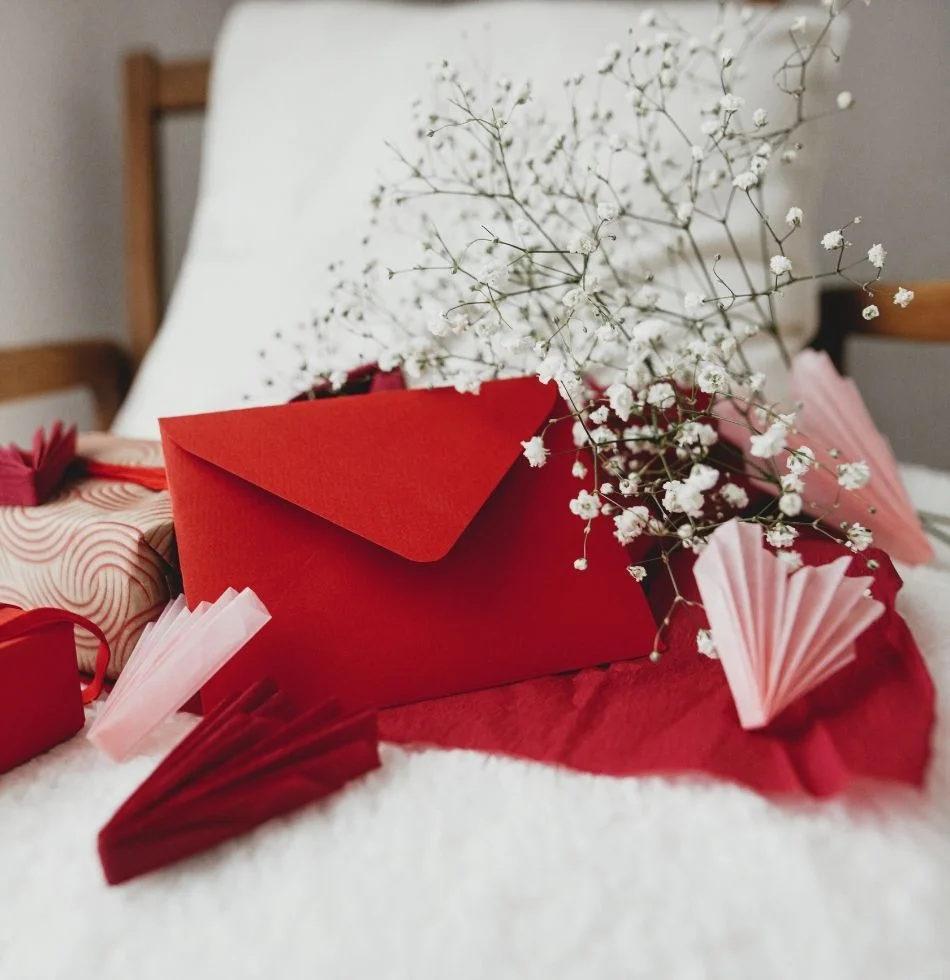 red envelop atop a cushion seat with flowres and other gifts and paper hearts