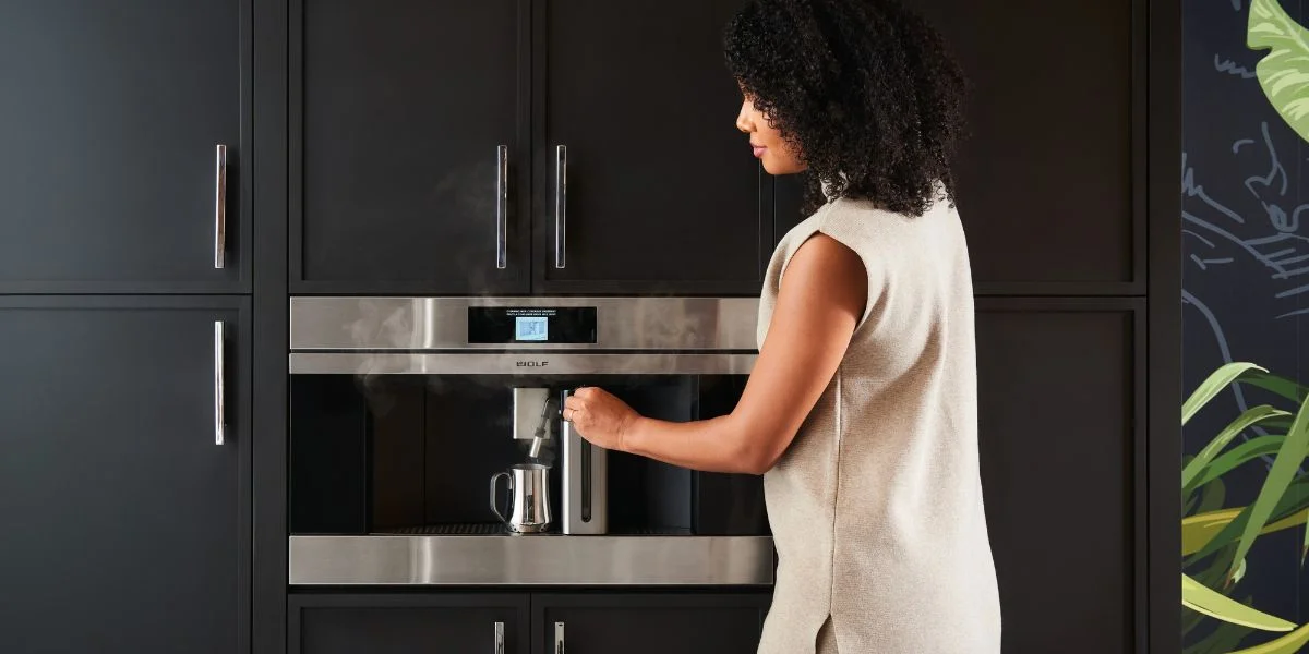 A woman using a Wolf built-in coffee maker and its dairy system to craft a beverage