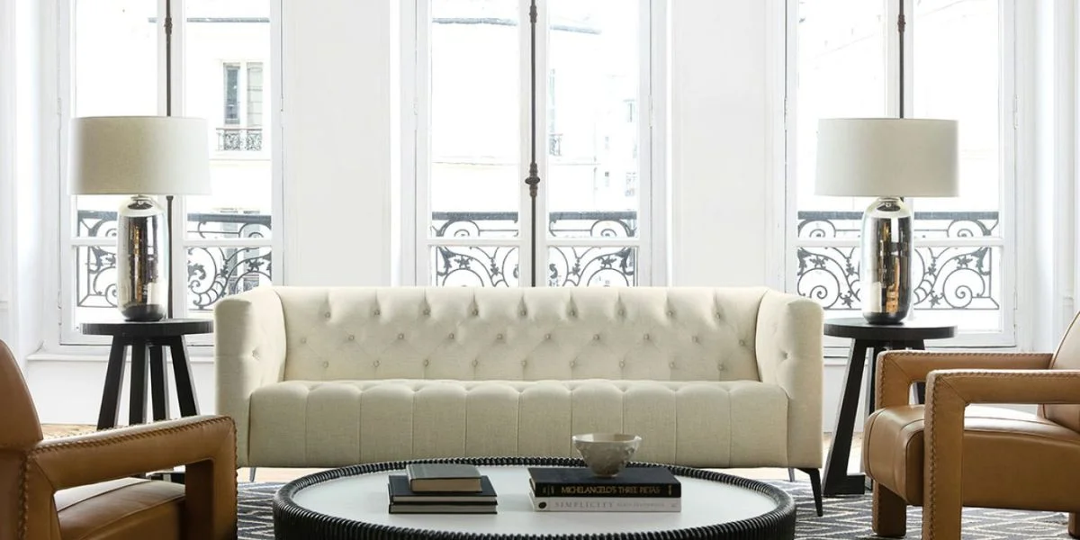 A finished living room complete with a tufted white sofa, coffee table, side tables and chair.
