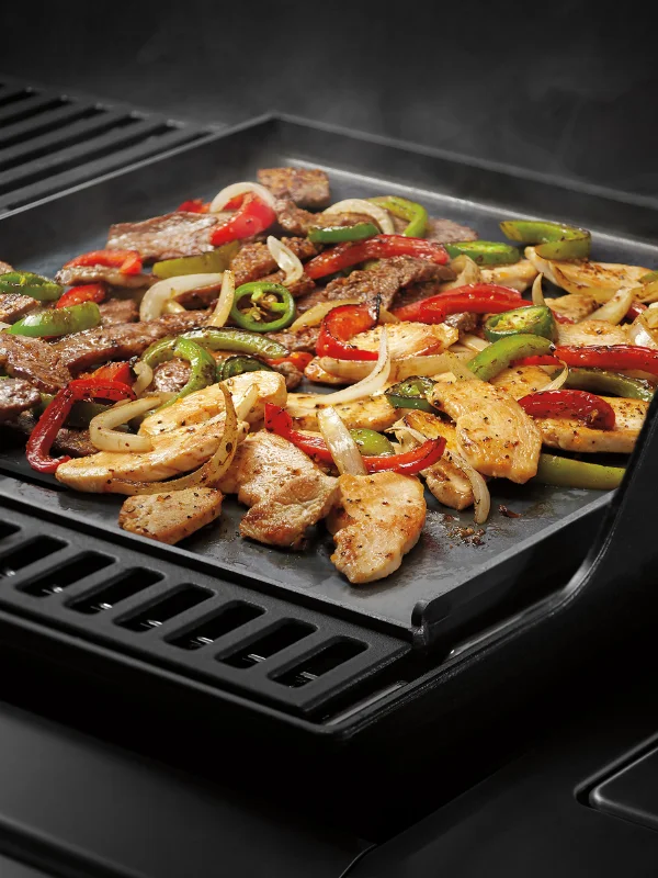 Tight shot on a grill baset on the grates with nachos in them and a hand sprinking cheese