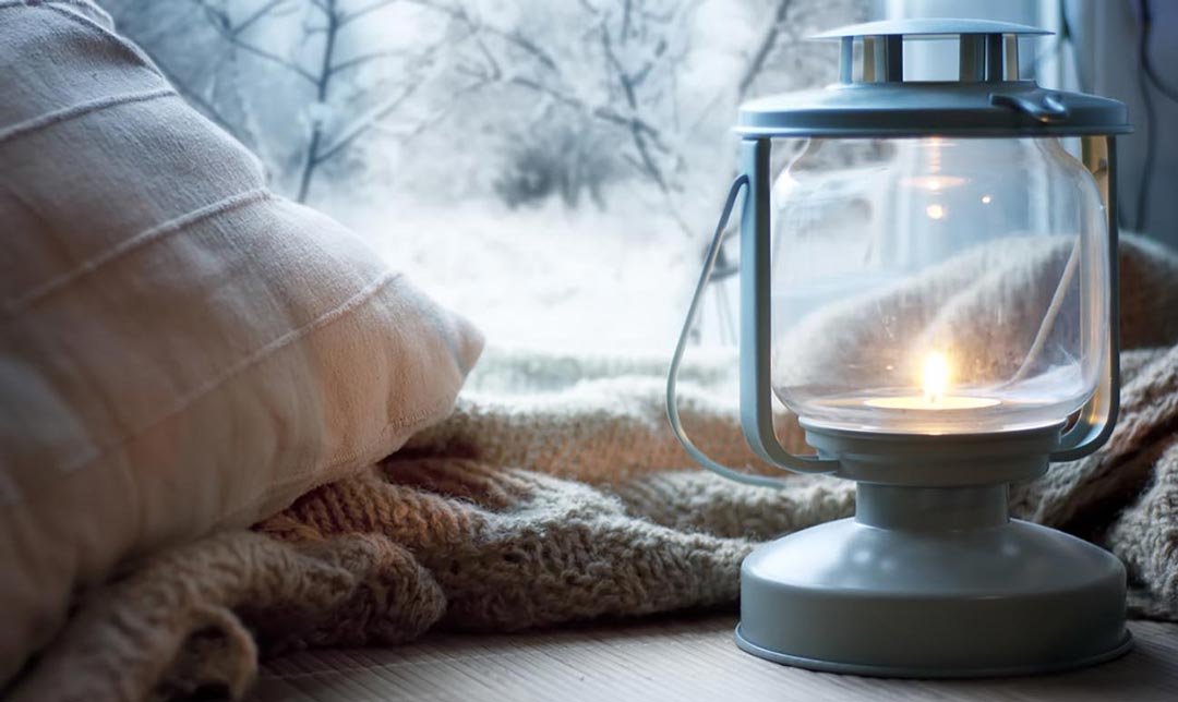 Home lantern lit in front of window with snow in background