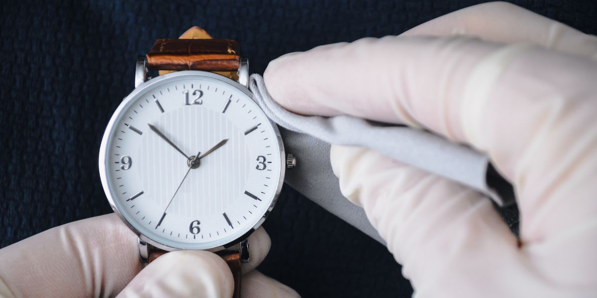 gloved hand wiping watch with a cleaning cloth