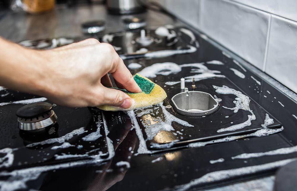 Person using cleaning products on gas stove top