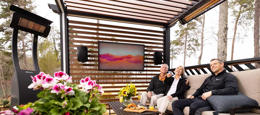 A black outdoor heater standing on a patio warming up three people as they watch their outdoor TV.