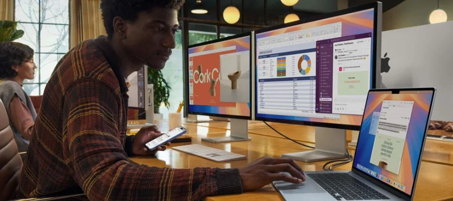 A man at a desk with two monitors as well as the MacBook Air. All three screens are lit and the MacBook is open