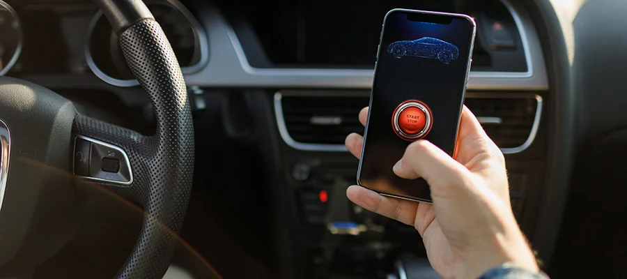 Someone sitting in the drivers seat of a car with a smartphone in his hand open to a remote start app to start/stop his vehicle