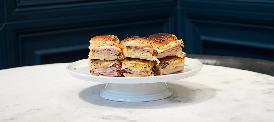 The finished ham and cheese sliders sitting on a white serving platter on a marble table