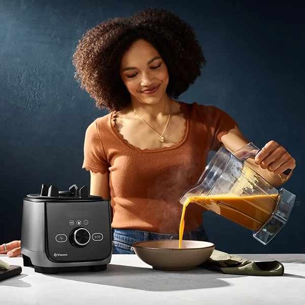 A woman pouring hot soup from the Vitamix Ascent X4 blender into a bowl