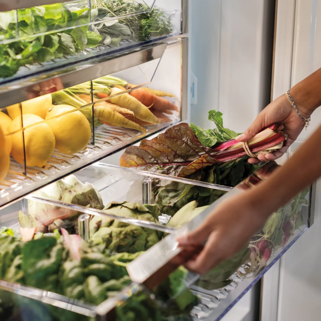 Close-up of a person opening a Sub-Zero refrigerator, showcasing a detailed vegetable and fruit drawer