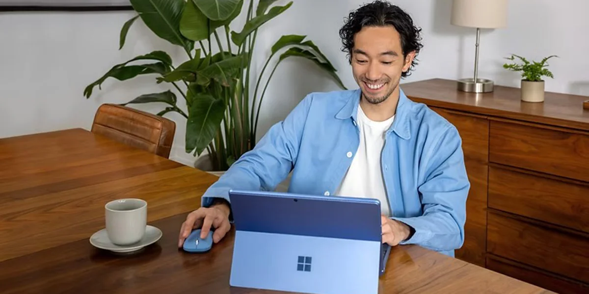 A man smiling with a windows surface pro laptop, keyboard and mouse