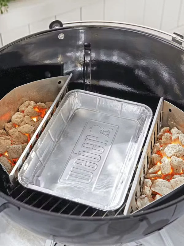 An aluminum weber drip pan placed in a weber charcoal grill