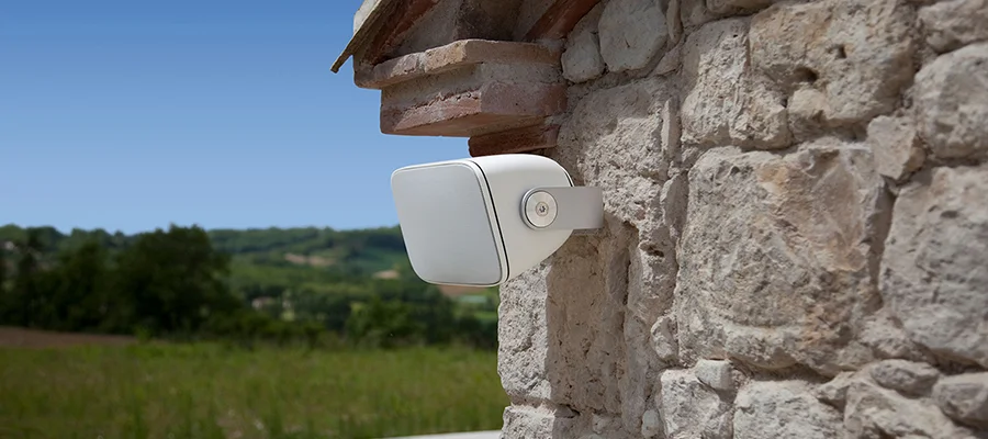 A white outdoor speaker mounted to the exterior stone wall of a home