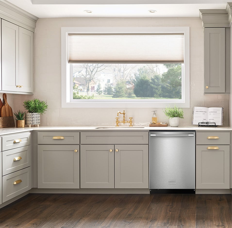 Modern kitchen with cream color cabintry outfitted with golden hardware and a stainless steel frigidaire professional built in dishwasher