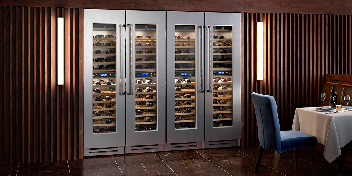 Four silver wine refrigerators next to each other installed in a wood-paneled wall