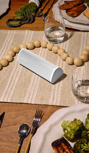 Sonos Roam 2 atop a dinind room table with a holiday wood bead garland placed in the middle of the table while dinnerware sits around