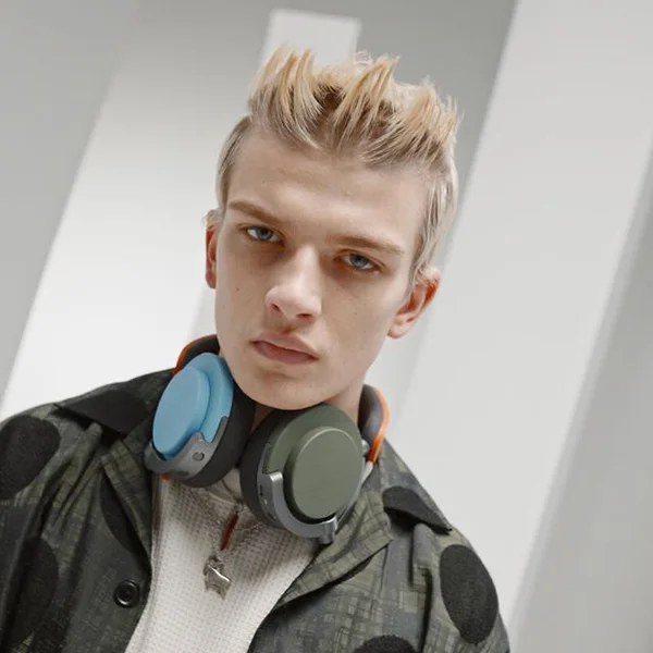 A man wearing a pair of Dyson OnTrac headphones around his neck with one blue ear cap and one green ear cap
