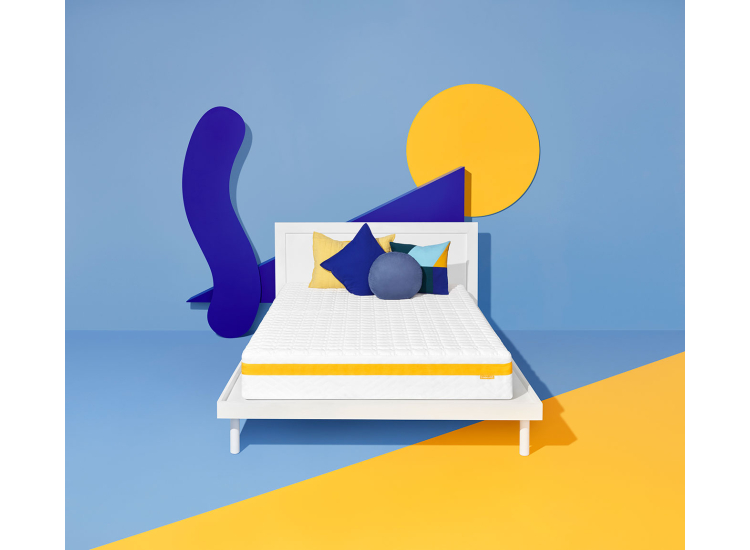 Overhead shot of a white mattress in a blue-and-yellow product display layout.