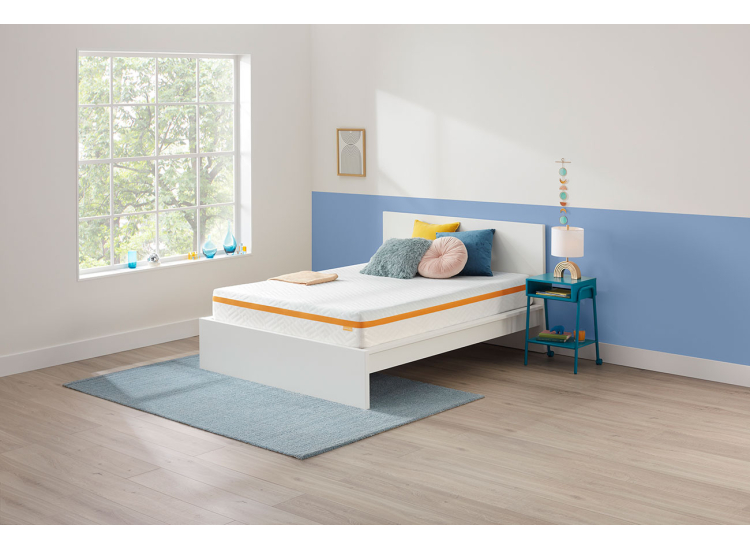 Side view of a white mattress with orange trim, displayed on a bed frame in a bright blue and yellow kids bedroom setup