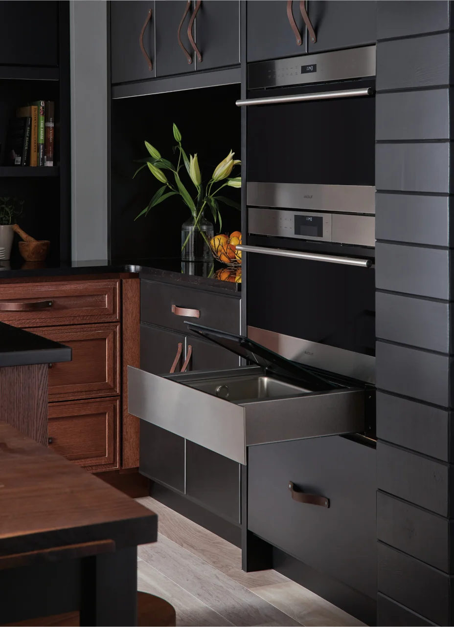 Stylish kitchen showcasing black cabinetry, warm wooden countertops, and a Wolf warming drawer for optimal food preparation