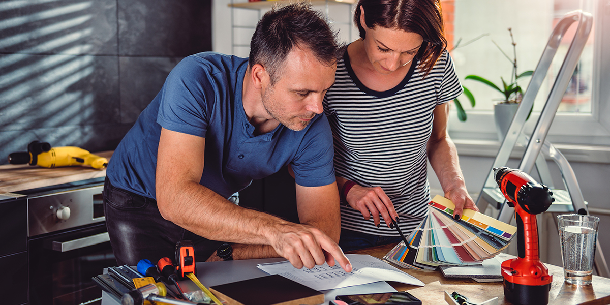 A man and a woman looking over a kitchen blueprint and colorful paint swatches