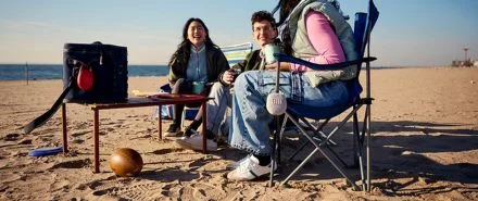 A group of friends talking on the beach while listening with two JBL Clip 5's.