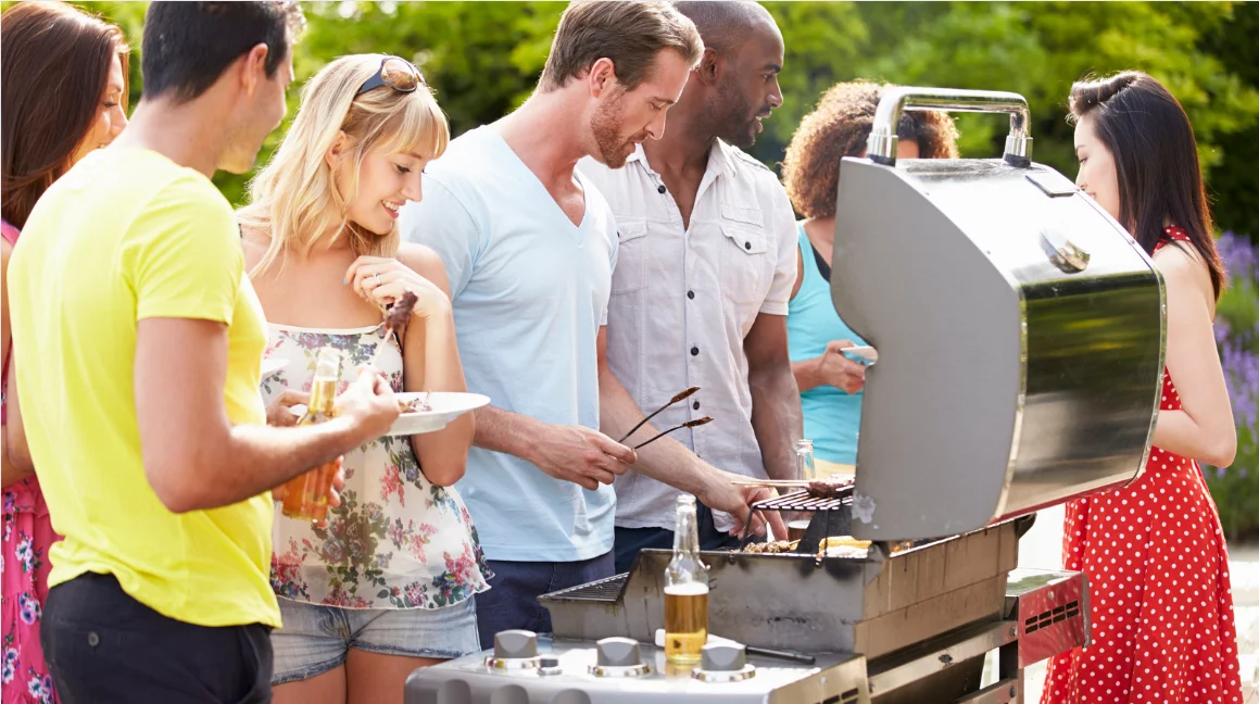 A group of people gathered around a man grilling
