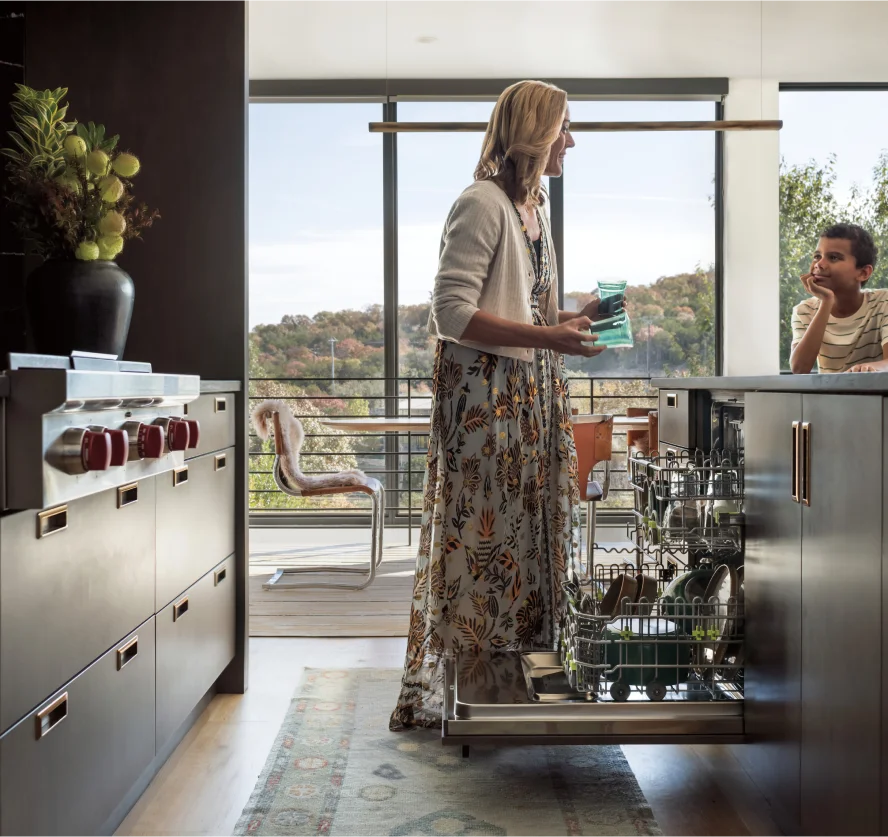 A woman stands in a modern kitchen featuring a built-in cove dishwasher and a Wolf range in the background