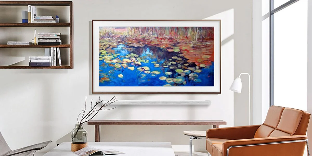 An art TV above a white soundbar in a living room with a leather sofa. The TV showcases a nature scene with lily pads on water.