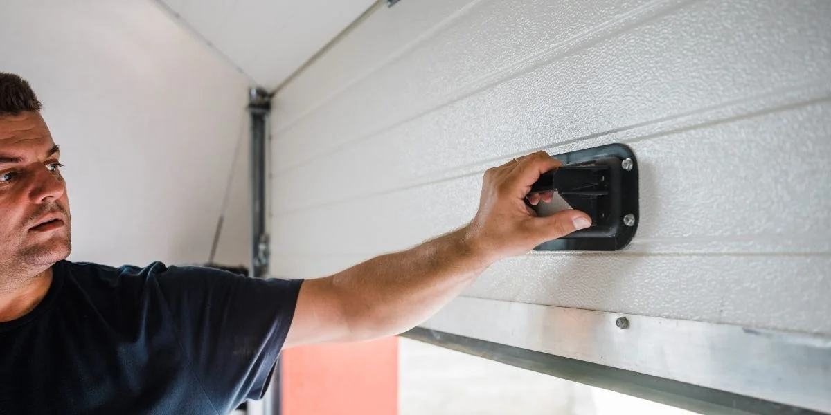 A man closing a garage door manually via the handle.