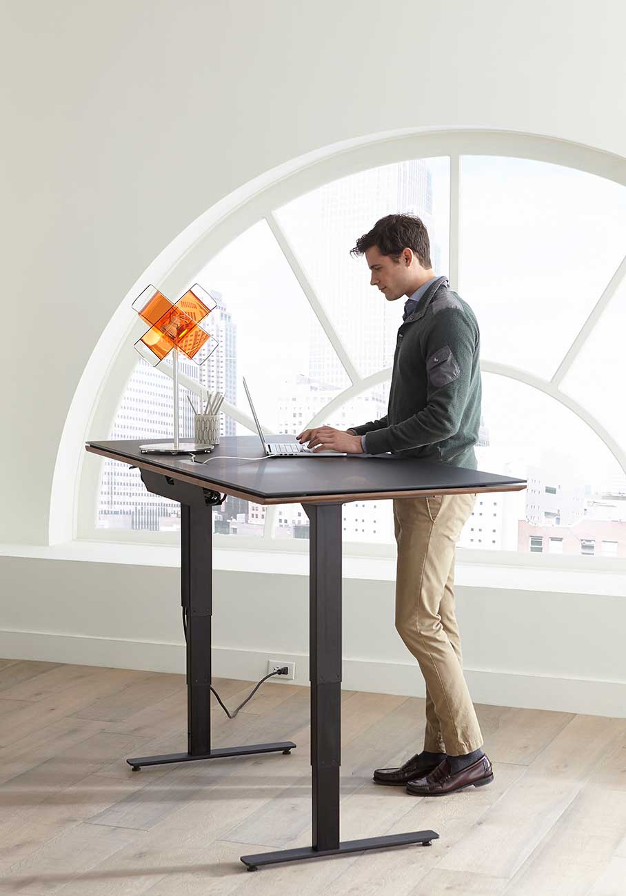 Lifted view of bdi natural walnut lift desk with model standing in office 