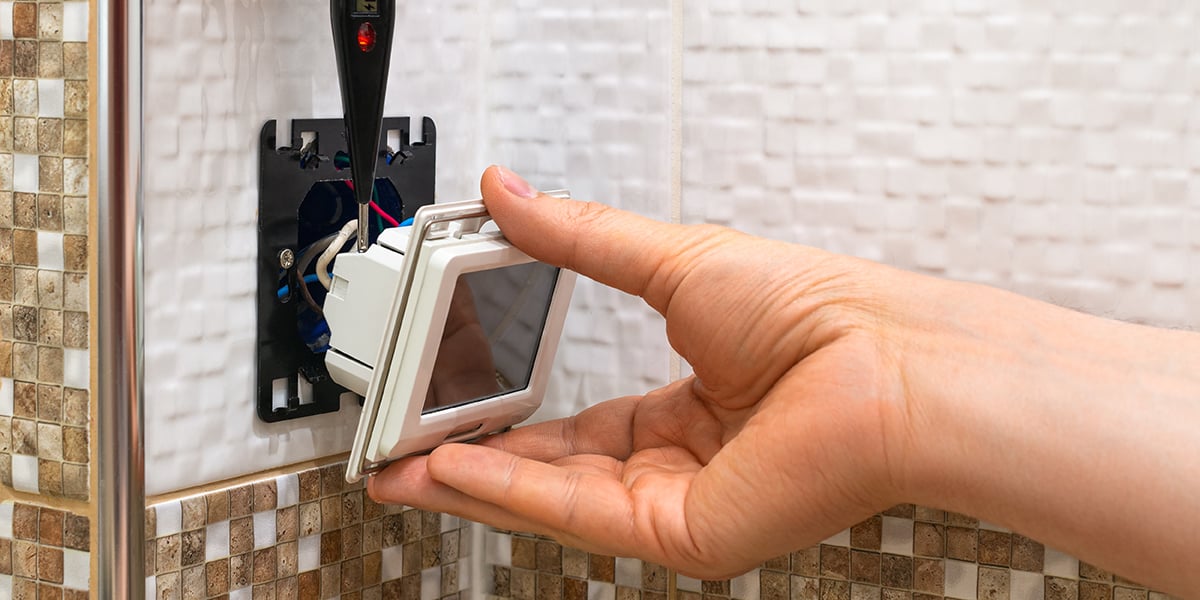 A person disconnecting a thermostat from the wall to expose the wires