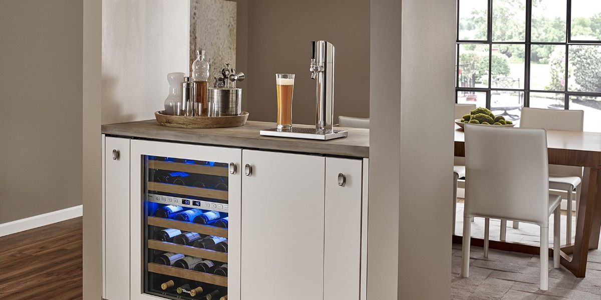 A built-in kegerator with a glass of beer on top of it, installed next to a beverage center