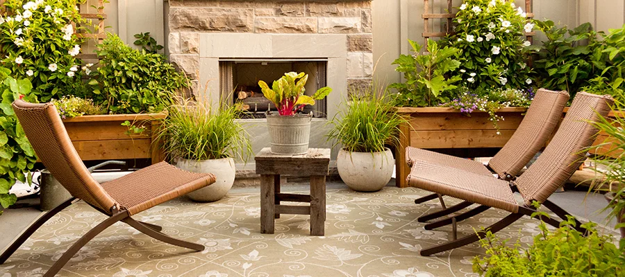 An outdoor patio with three seats, surrounded by various plants and greenery.