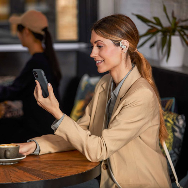 A women sitting in a cafe looking at her phone and wearing a beige pair of headphones as a Mother's Day gift.