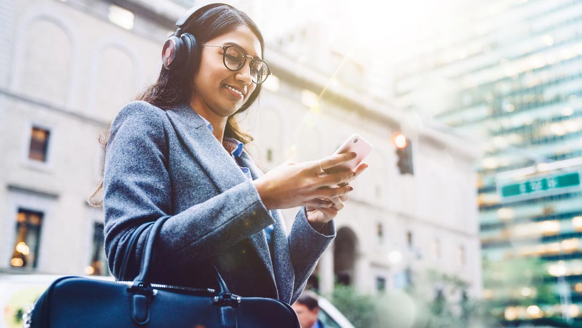 Woman holding a smartphone and wearing headphones walking in a metropolitan area