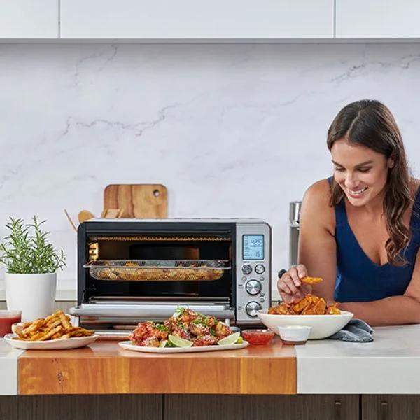 Woman reaching into a bowl of air fried fries beside the Breville Smart oven Air Fryer Pro
