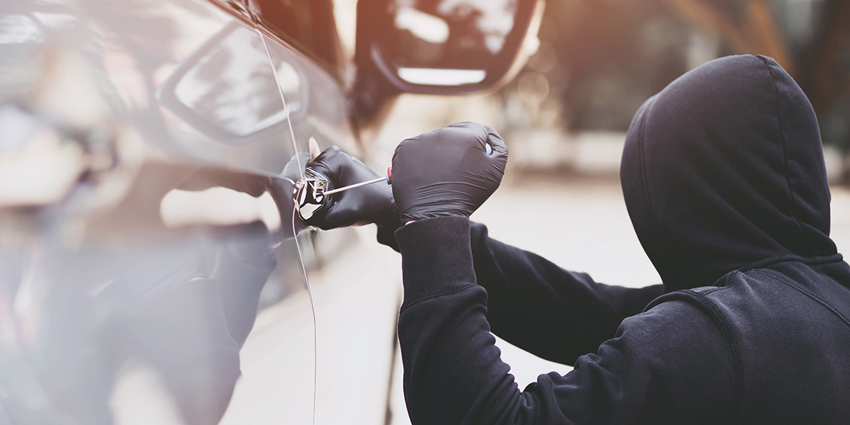 A person in a black hooded sweater and black gloves using a screwdriver to break into a vehicle