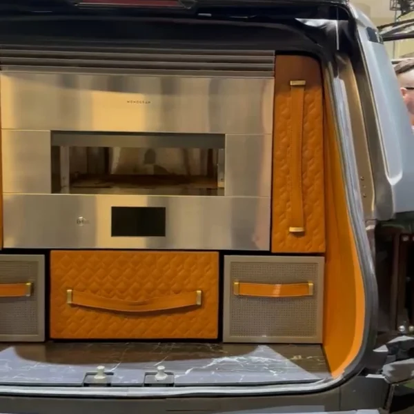 The open trunk of the Monogram GX vehicle featuring a built-in wall oven and storage for other cooking tools