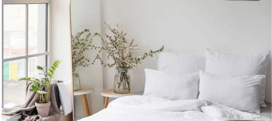 A minimalist bedroom with a comfortable bed, an oversized mirror and plants near the window