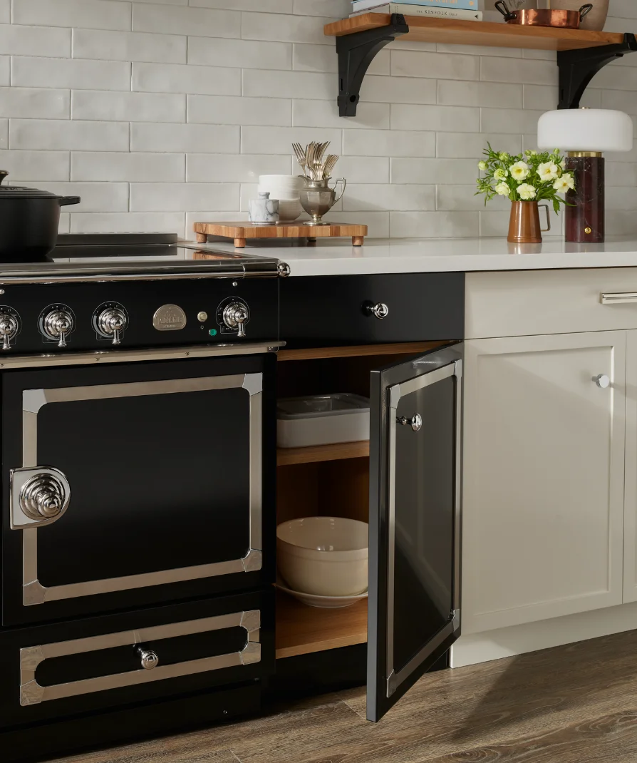 Black La Cornue range with open cabinet door showing bowl storage beneath a wood shelf