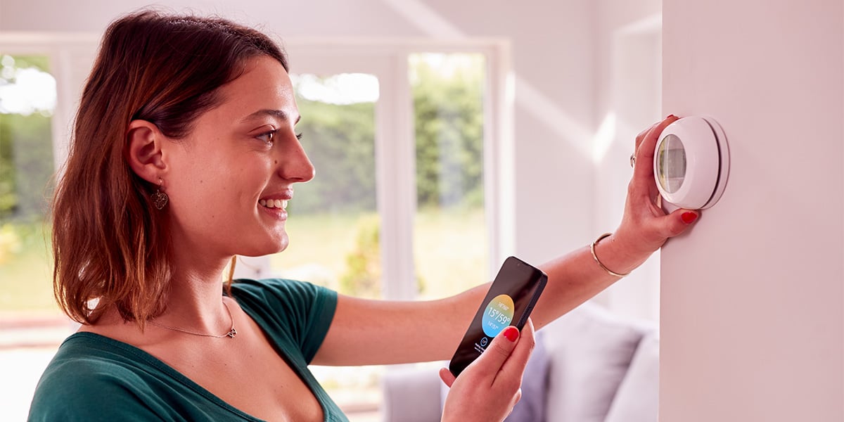 Woman programming her smart thermostat and connecting to her smartphone.