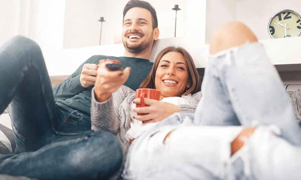 Two people watching TV on a sofa with coffee