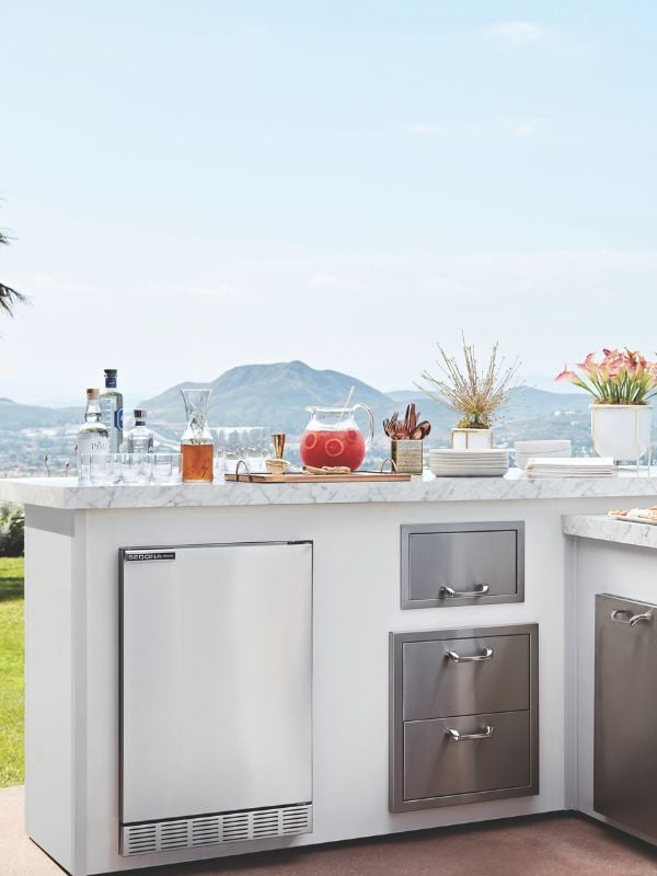 A detailed off centered shot of an outdoor bar with built in refrigerator, warming drawers and cocktail on the countertops