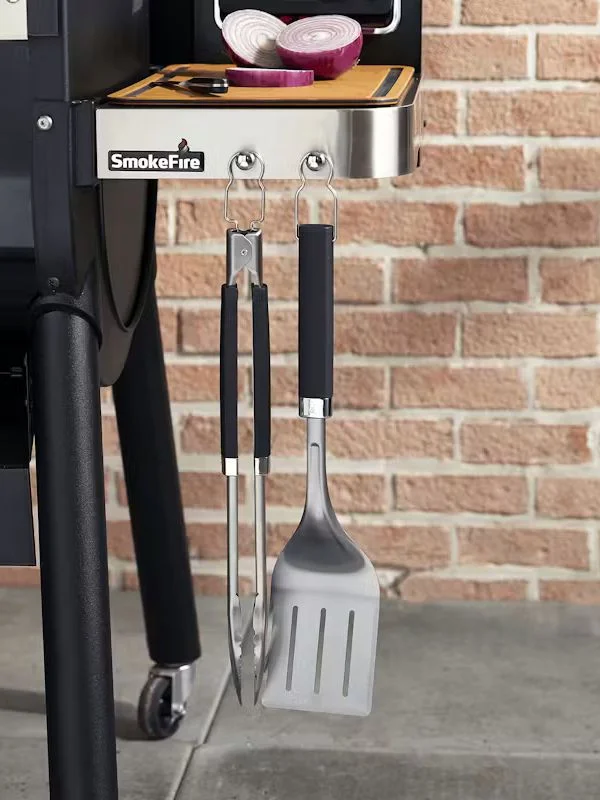 Tight shot on a weber tong and spatula hanging off a smoke fire attachement of a grill
