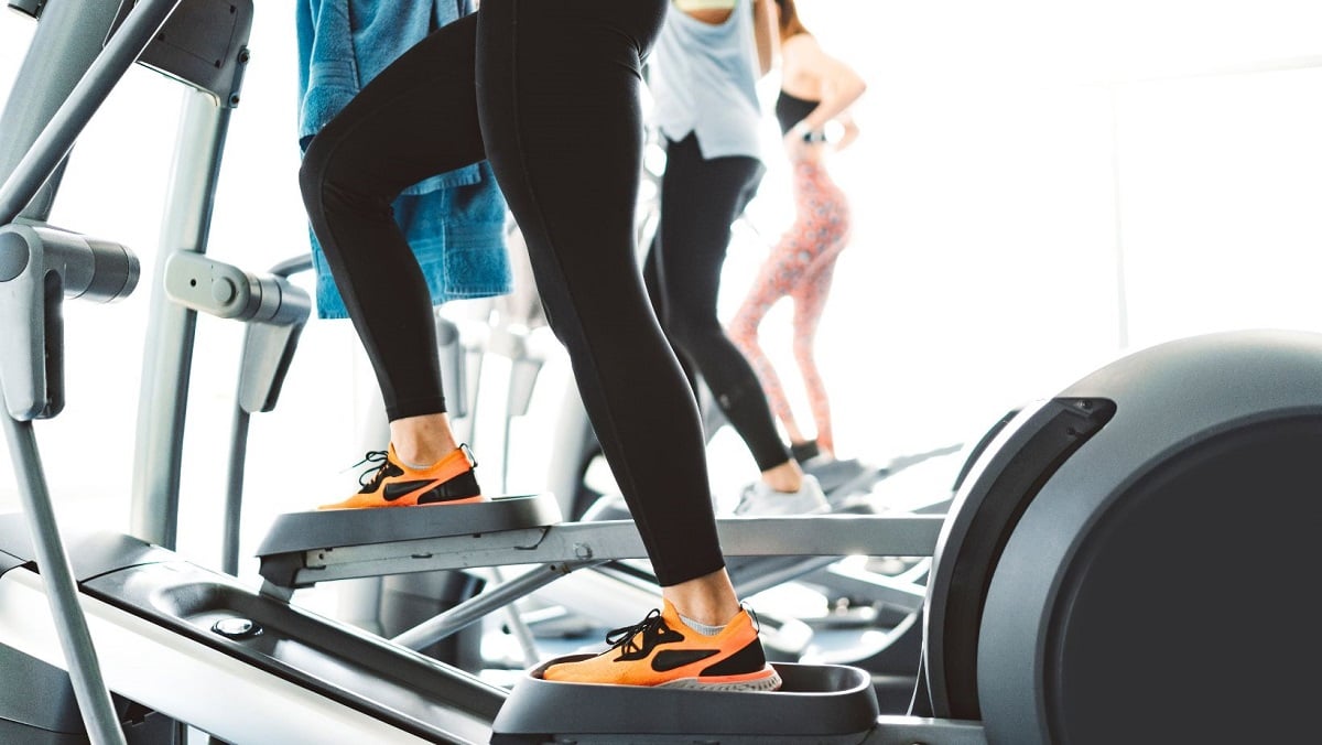 Close-up of a person's legs on an elliptical. They are wearing cropped black leggings and black and orange gym shoes.