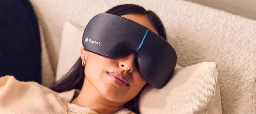 A woman using the Therabody SmartGoggles in bed with a smile on her face.
