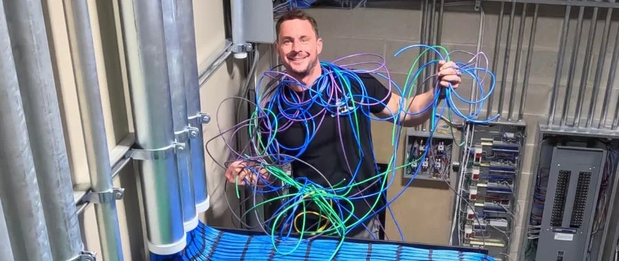 Craig Donovan having fun with wiring behind the scenes at Abt; he's wrapped up in colorful scrap wires and smiling at the camera
