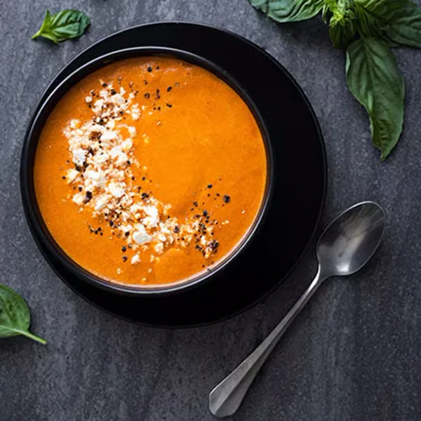 Vitamix's roasted red pepper soup in a bowl with garnishes and a spoon