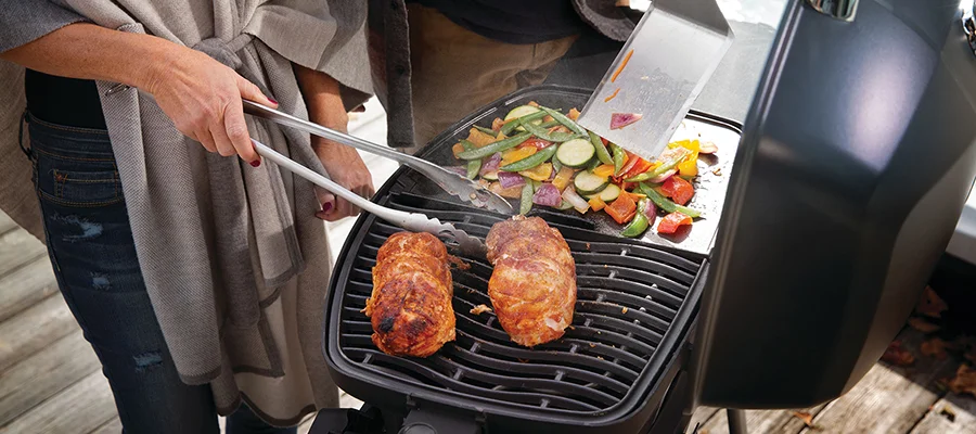 A couple cooking chicken and vegetables on a black grill together