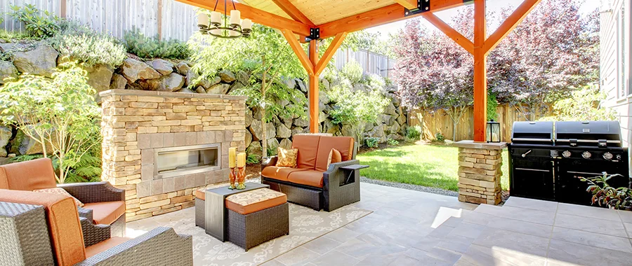 A backyard porch with chairs, a coffee table, a fireplace and a black grill